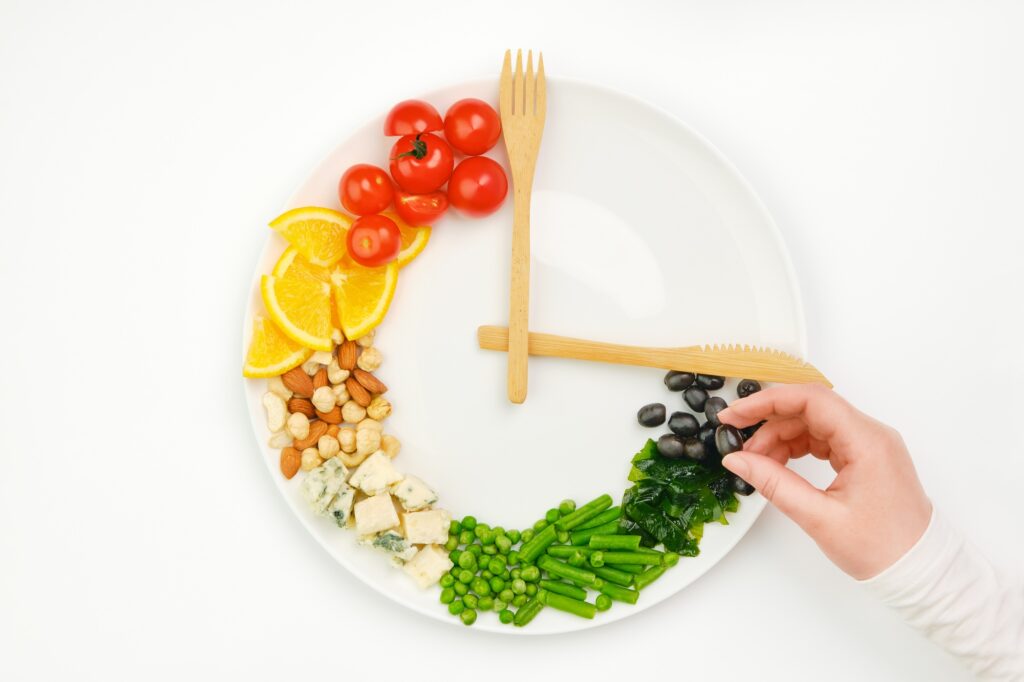 Colorful food and cutlery arranged in the form of a clock on a plate. Intermittent fasting