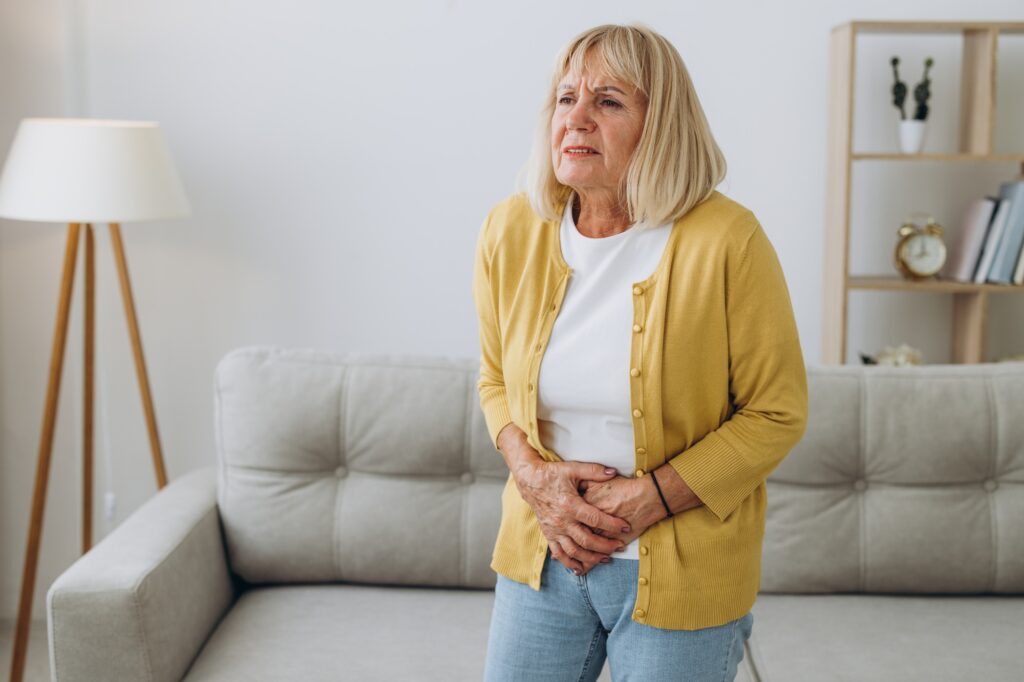 Senior blonde woman wearing casual clothes with hand on stomach in living room