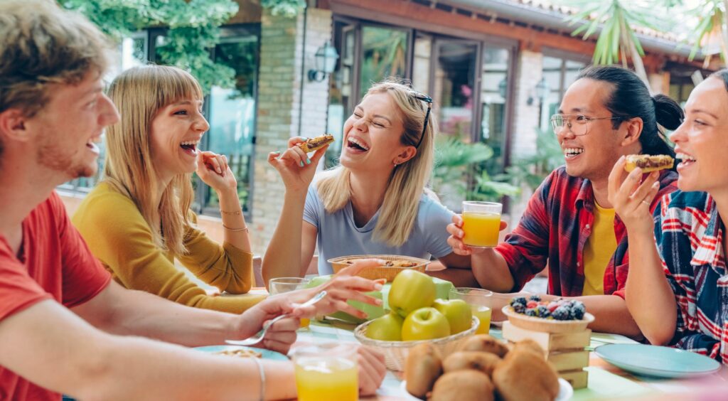 Happy young people eating healthy food at farm house picnic